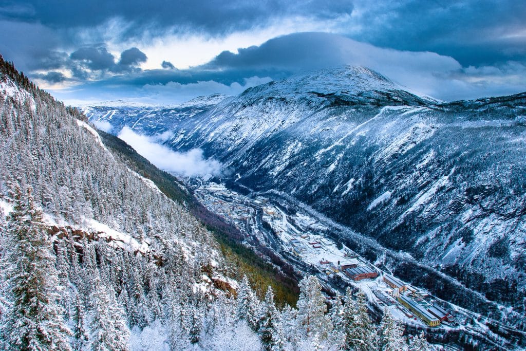 a snowy mountain range with trees and clouds